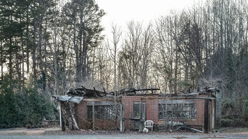 A fire-damaged brick house with a collapsed roof among East Texas pines
